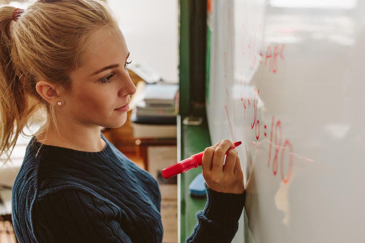 Una profesora escribe en una pizarra