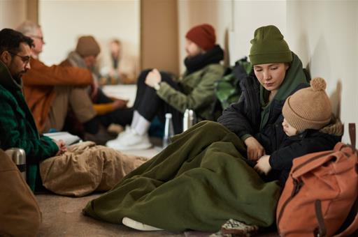 Madre con su hijo sentados en el suelo de una habitación junto a otros refugiados.